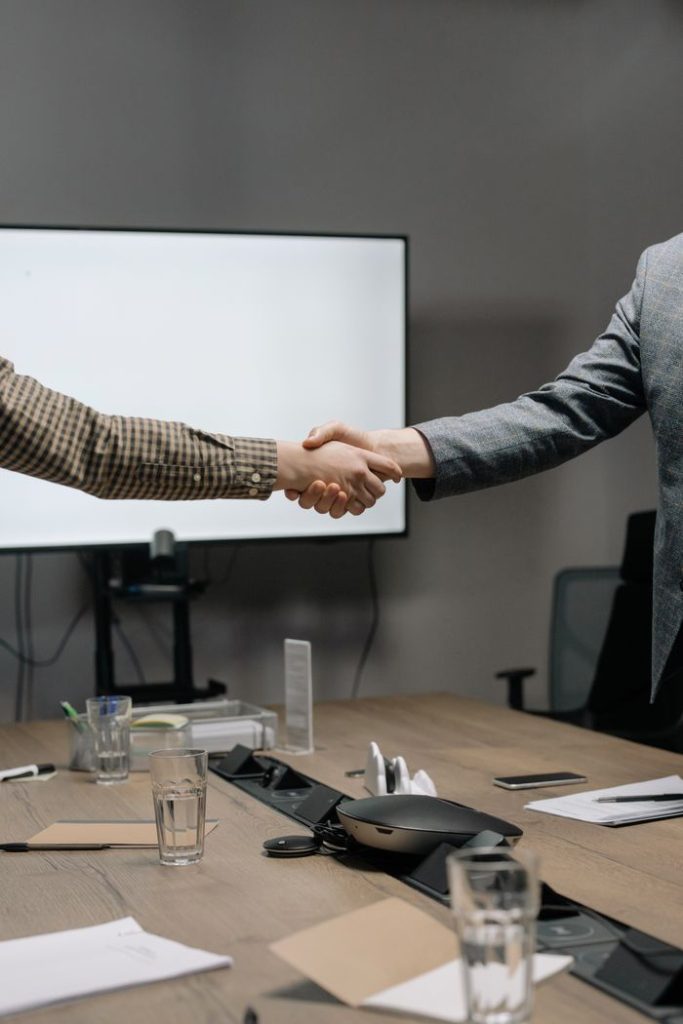 About Two business professionals shaking hands in a modern meeting room, symbolizing successful collaboration.